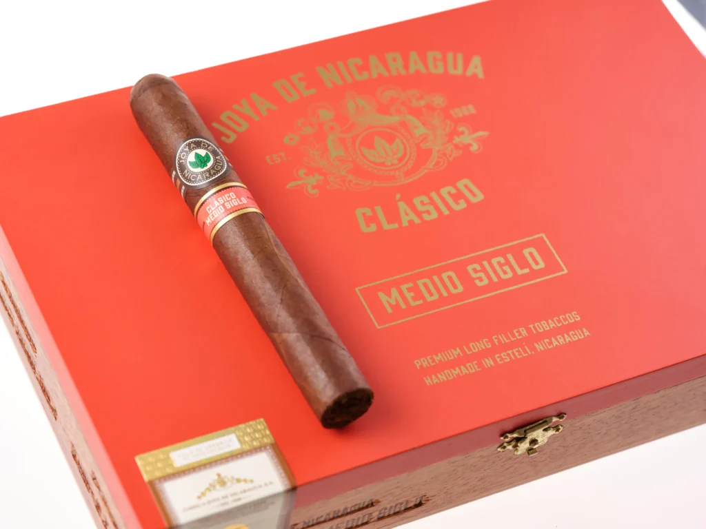 Red box labeled “Joya de Nicaragua Clásico Medio Siglo” with a premium cigar resting on top, showcasing handmade long filler tobaccos.