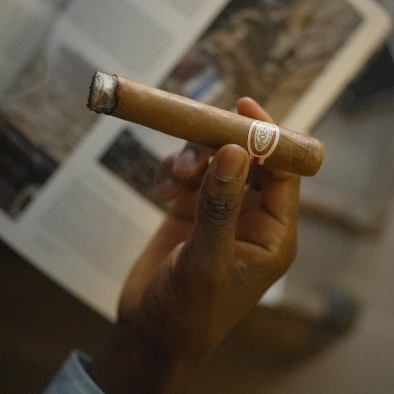 A person holding a 20 ACRE FARM cigar between their fingers
