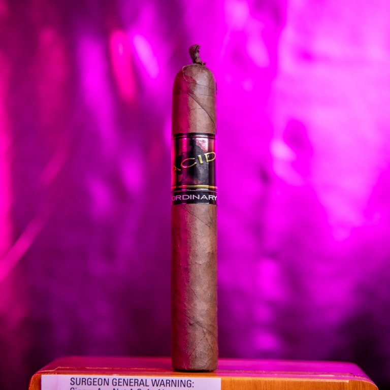 Drew Estate Acid Morado cigar standing tall against a vivid purple background, showcasing its dual-band design.