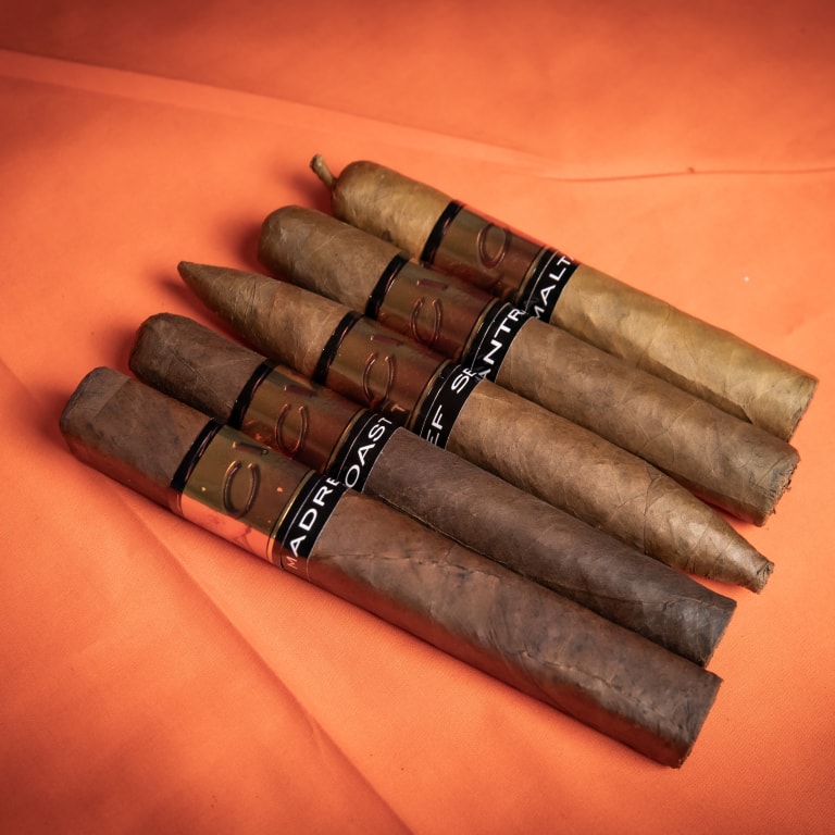A fanned arrangement of five Drew Estate Acid Subculture Cigars, showcasing various wrapper shades from light tan to dark brown.