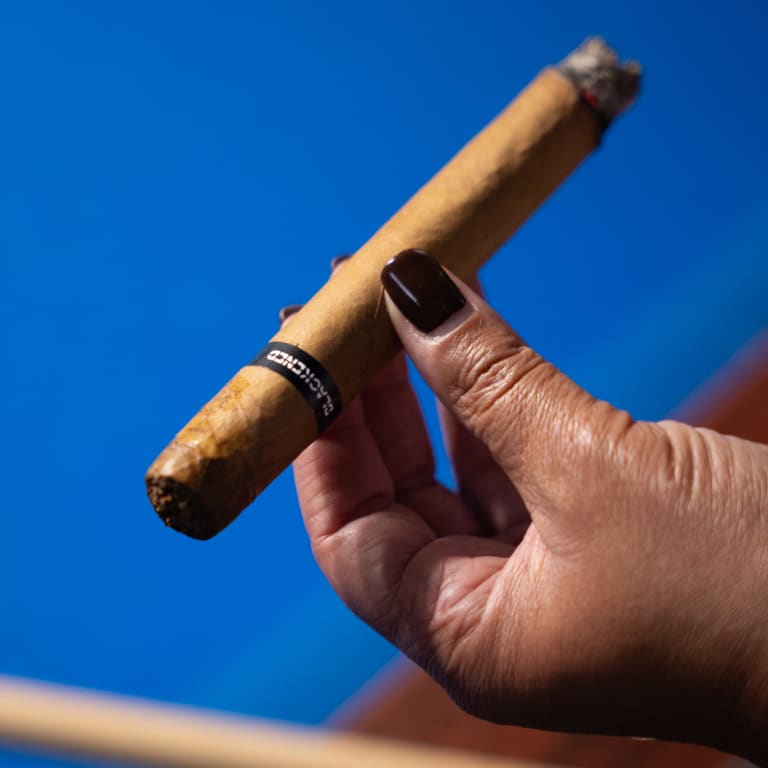 hand holding a blackened cigar upon a clear blue sky