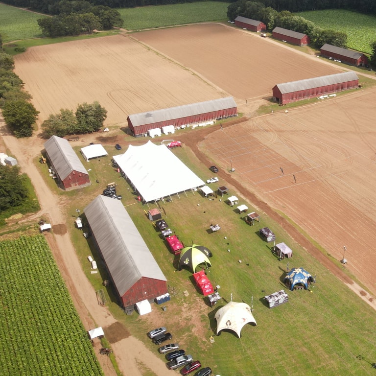 Aerial view of the Connecticut Barn Smoker Event featuring large white tents, rustic barns, and parked vehicles surrounded by plowed fields and farmland