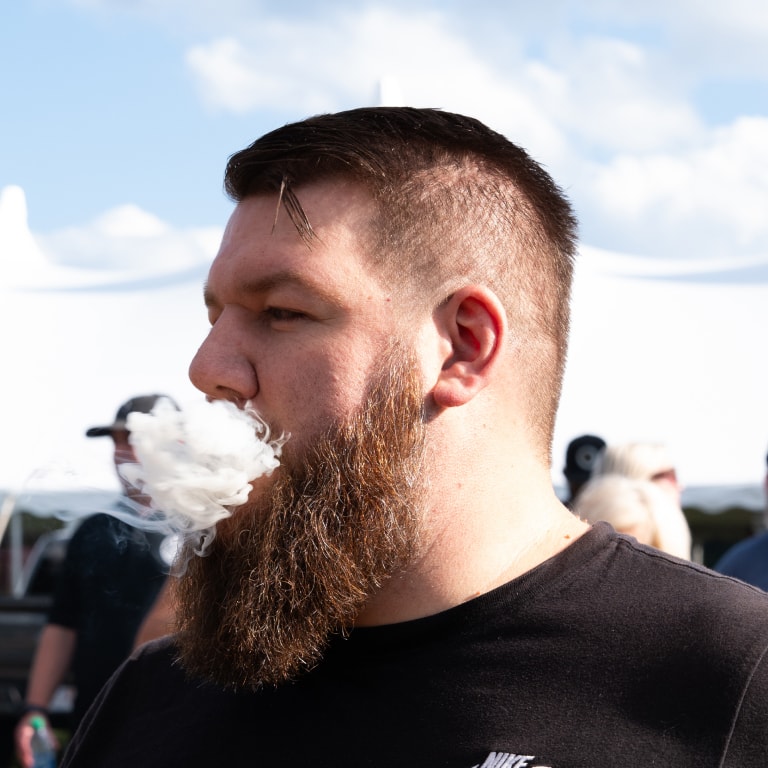 Bearded man in a black Nike shirt stands outdoors under a partly cloudy sky at the Connecticut Barn Smoker Event, surrounded by fellow attendees.