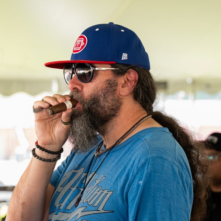 Attendee at the CONNECTICUT BARN SMOKER Event smoking a LIGA PRIVADA cigar in a relaxed setting, dressed in casual blue attire.
