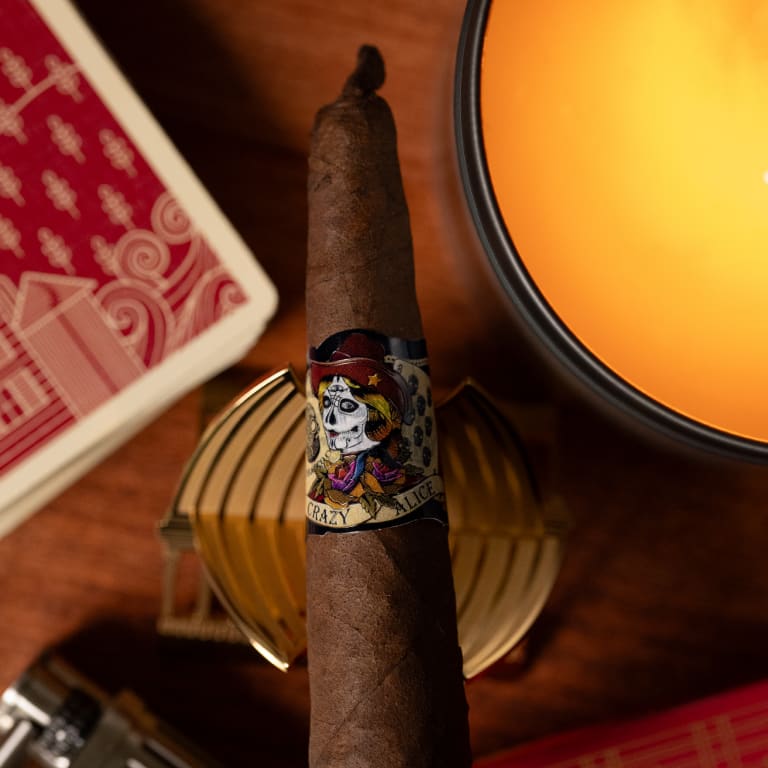 A Deadwood Crazy Alice cigar rests on a table, illuminated by the warm glow of a nearby candle