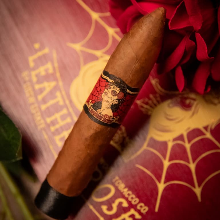 deadwood leather rose cigar rests on a vibrant red rose, set against a soft, muted background that enhances its rich colors.