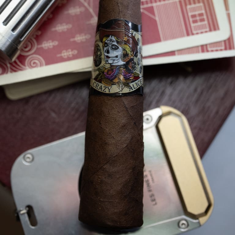 deadwood crazy alice cigar laying on top of playing cards on a wooden table