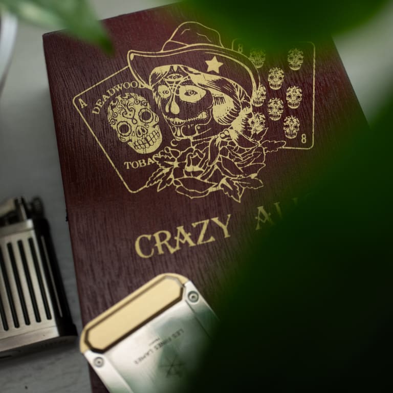 A wood surface featuring a gold cover adorned with a gold design, showcasing the Deadwood Crazy Alice logo