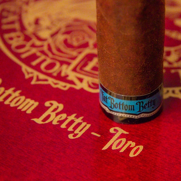 A Ddeadwood fatbottom betty cigar rests atop a red-covered book