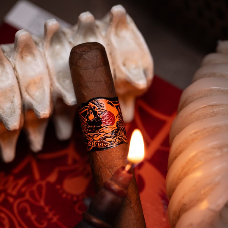 A Deadwood Sweet Jane cigar rests atop a bone beside a flickering candle