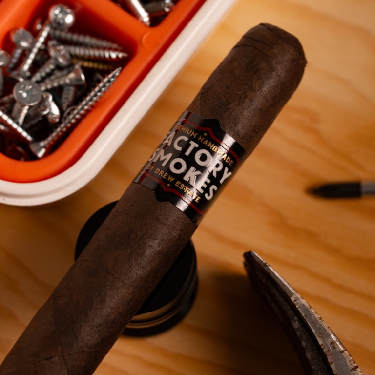 Factory Smokes Maduro cigar over a desk with some tools