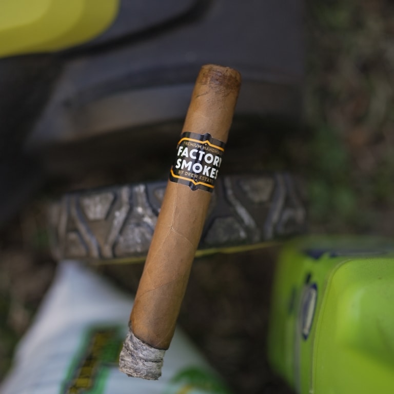 a Factory Smokes Shades cigar on a lawn mower