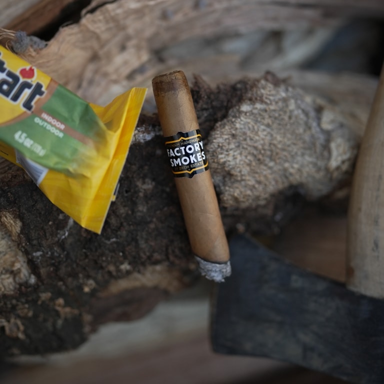 a Factory Smokes Shades cigar on a piece of wood and an axe.