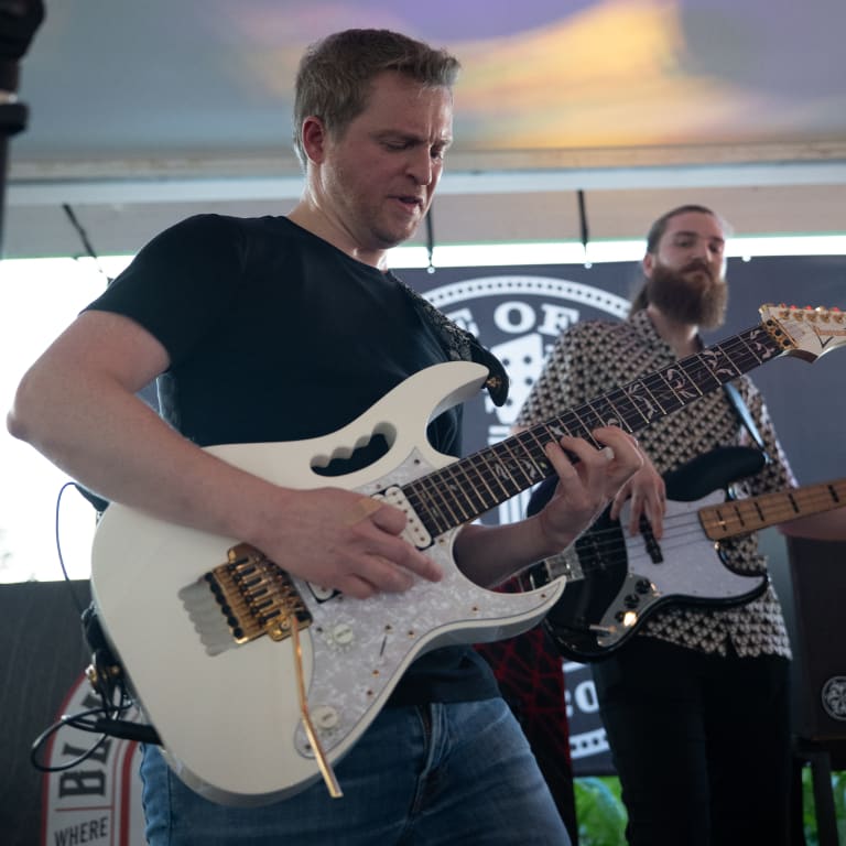 guitarist passionately plays a white electric guitar on stage, accompanied by a bassist in the background