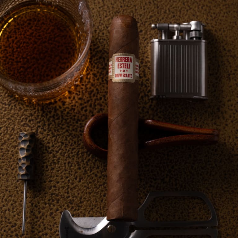 herrera esteli cigar laying by a glass of whiskey