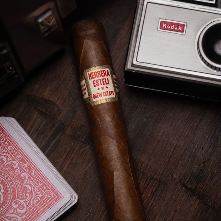 herrera esteli habano cigar laying between a camera and playing cards