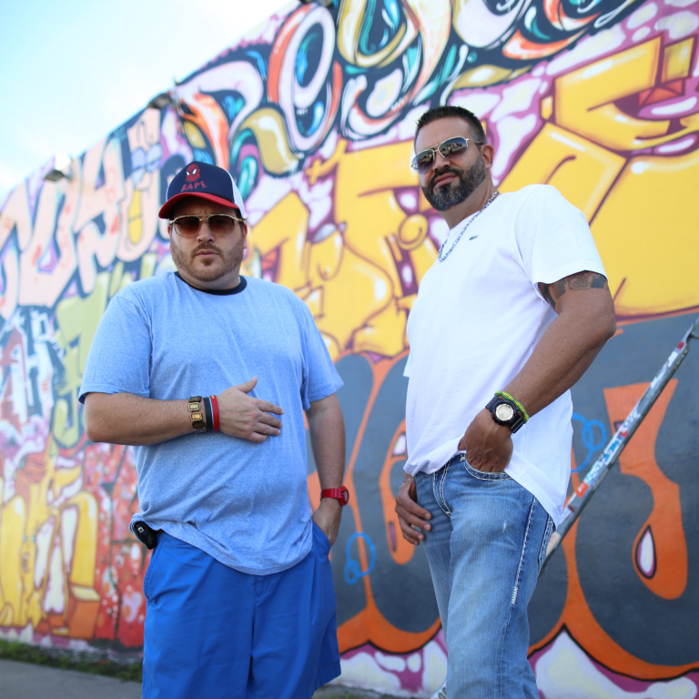 Willy Herrera and JD in front of a colorful graffiti wall
