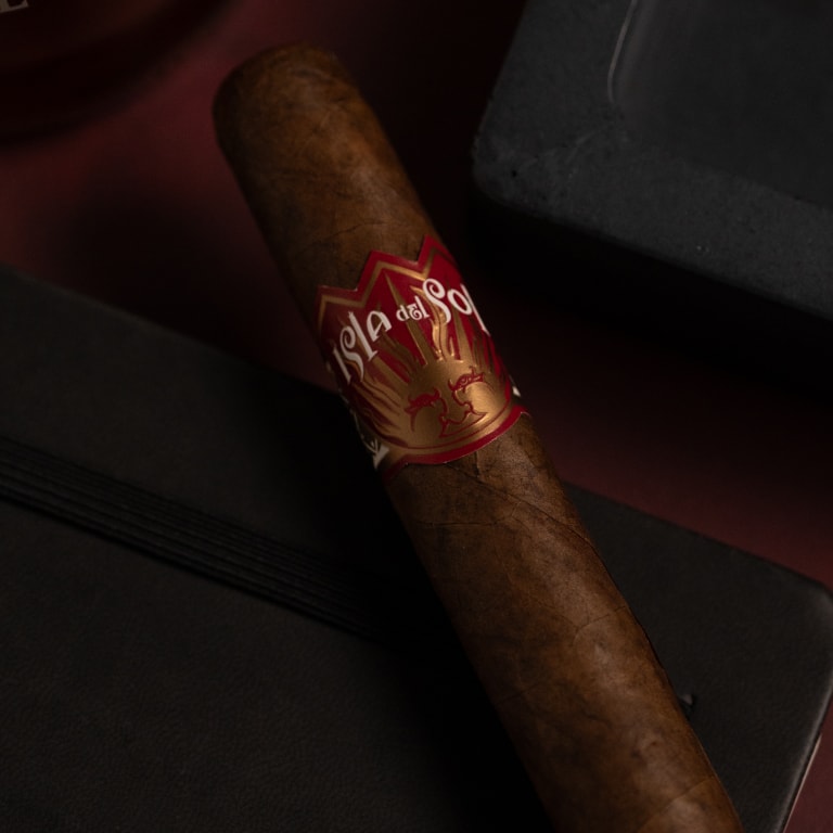 Isla del Sol cigar by Drew Estate resting on a dark notebook with an elastic band, showcasing its signature label.