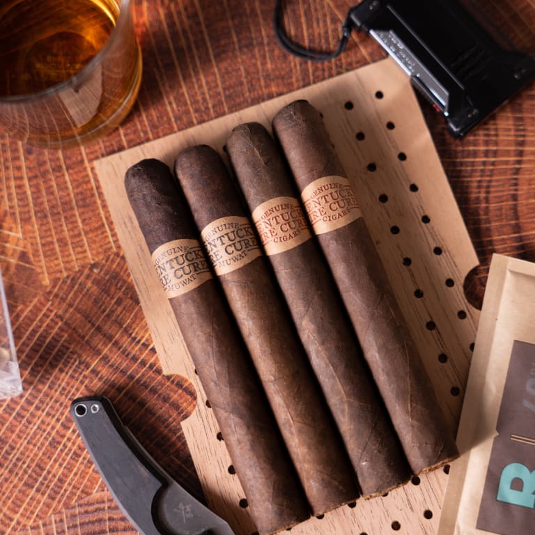 A rustic setting featuring four Kentucky Fire Cured cigars, a knife, a whiskey bottle, and a glass of whiskey on a wooden table