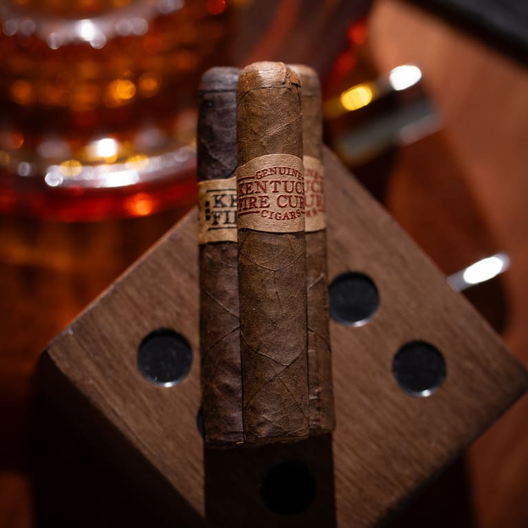 a rustic setting with three Kentucky Fire Cured Original cigars stacked on a wooden block