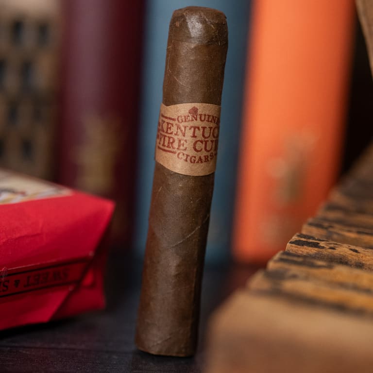 A kentucky fire cured original cigar rests atop a table beside a box
