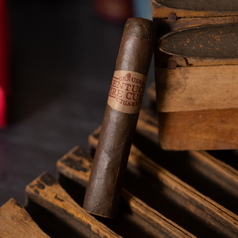 A kentucky fire cured sweet cigar resting on a wooden crate atop a wooden surface
