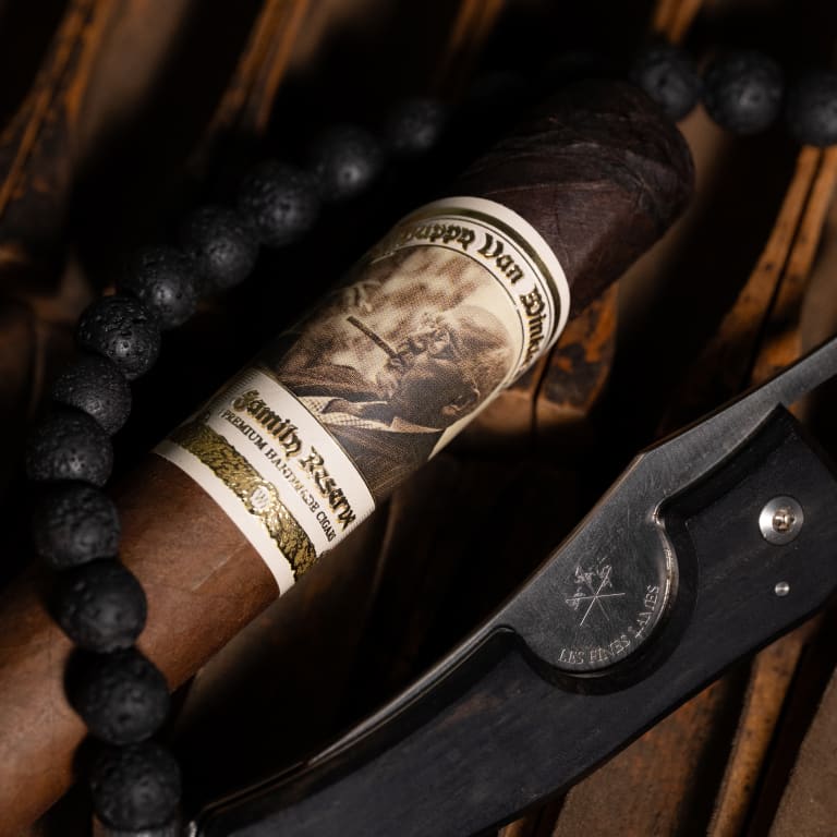 A pappy van winkle barrel fermented cigar and a knife resting on a rustic wooden table