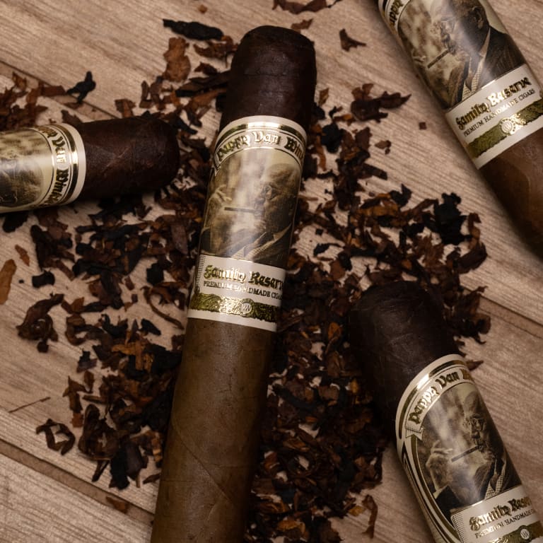 four Pappy Van Winkle barrel fermented cigars resting on a wooden table, surrounded by loose tobacco leaves