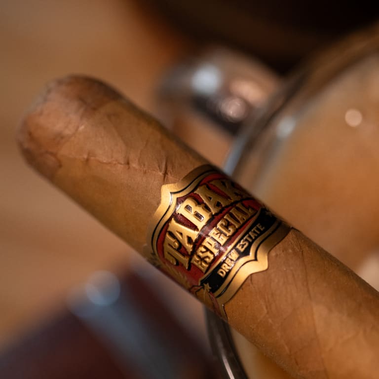 A Tabak Especial cigar rests elegantly on a glass, surrounded by a warm, inviting ambiance of a cozy lounge