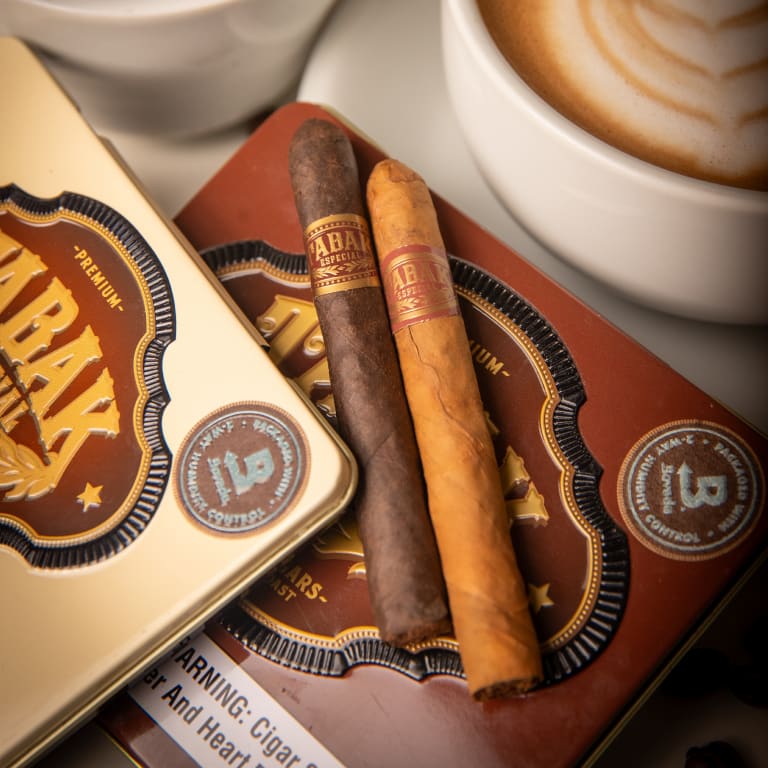 2 tabak especial cigars laying on a box by a cup of coffee