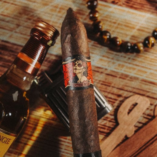 A Deadwood Leather Rose cigar rests on a wooden table beside a bottle of liquor