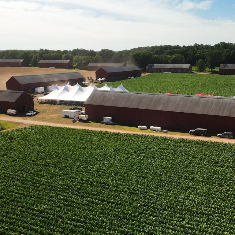 Aerial view of a vibrant field with a couple red barns nestled among the crops under a clear blue sky