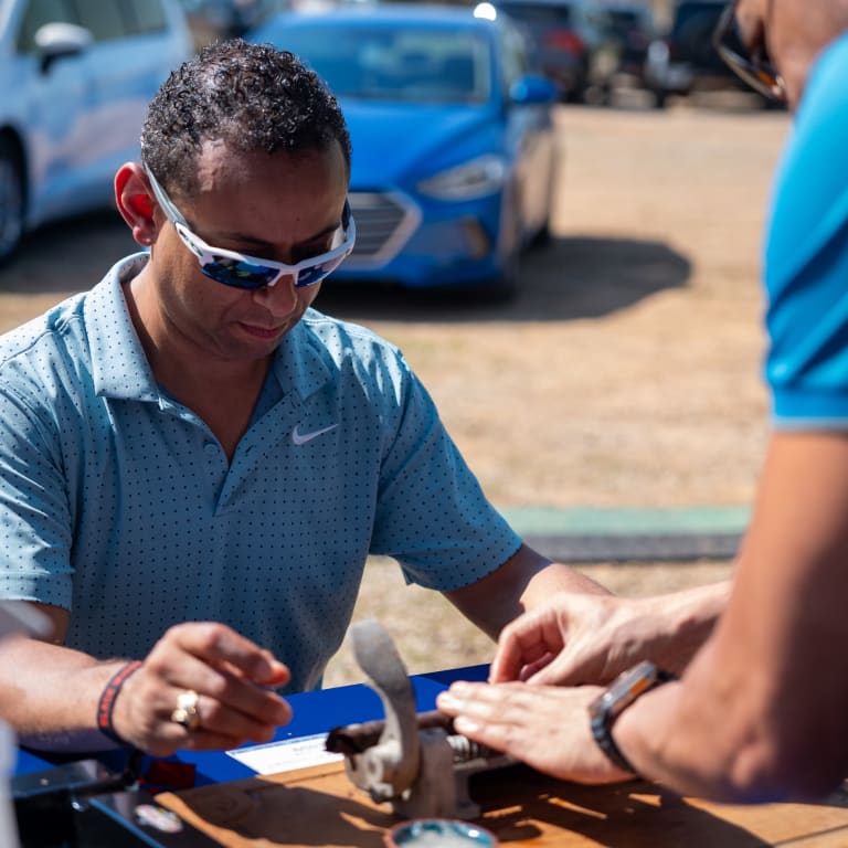 A man in sunglasses and a blue shirt is skillfully rolling a cigar