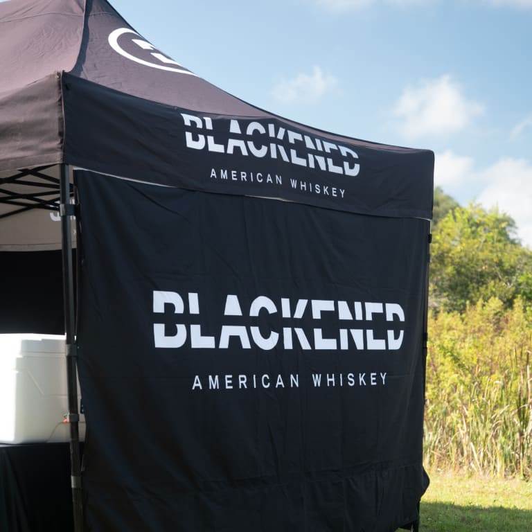 A tent featuring a blackbird design, promoting American whiskey, surrounded by nature