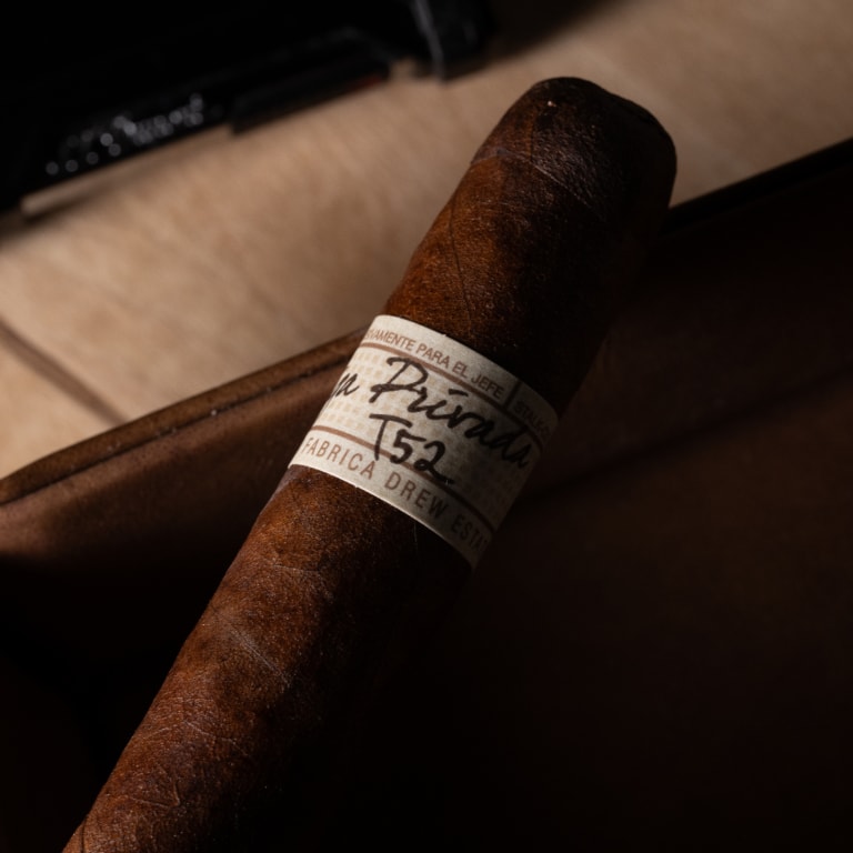 A Liga Privada T52 cigar positioned on a leather case, with a dark shadow
