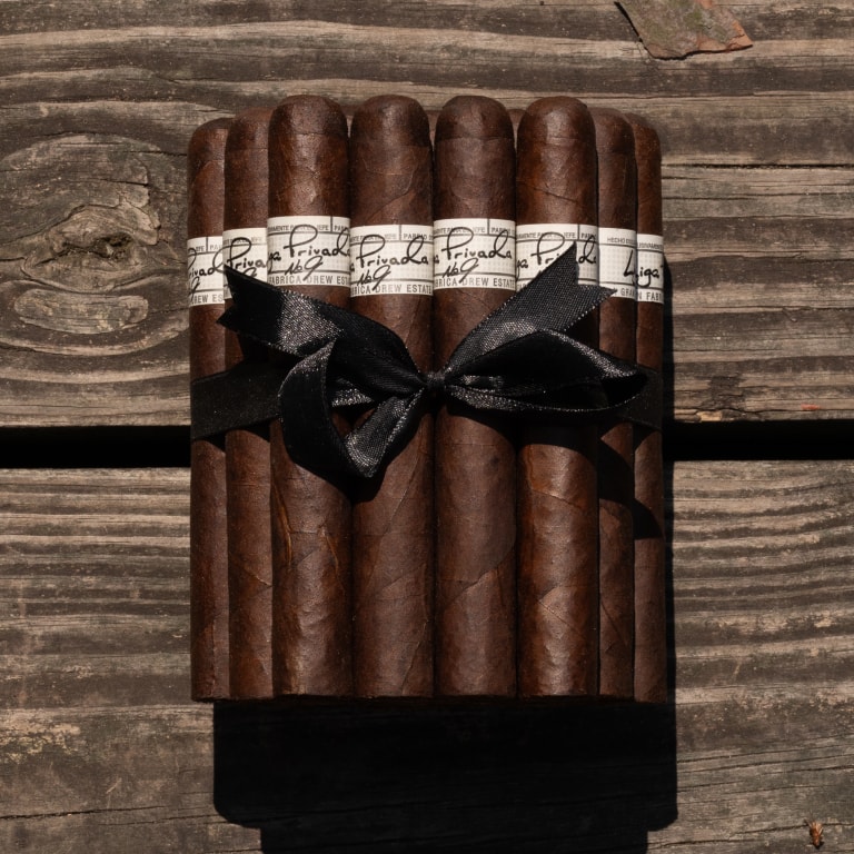 a bunch of Liga Privada cigars tied with a black ribbon on a wooden surface