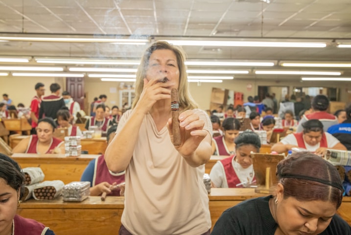 a woman smoking and holding a Factory Smoke cigar in a cigar factory