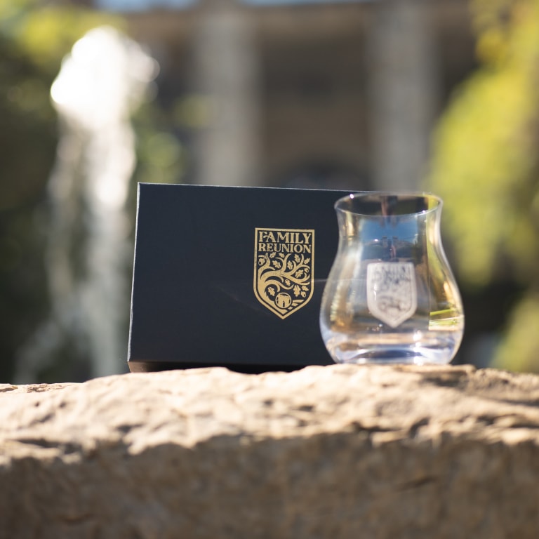 Close-up of a commemorative glass and box with gold 'FAMILY REUNION' emblems, resting on a rock with a natural backdrop from the Kentucky Castle Family Reunion.
