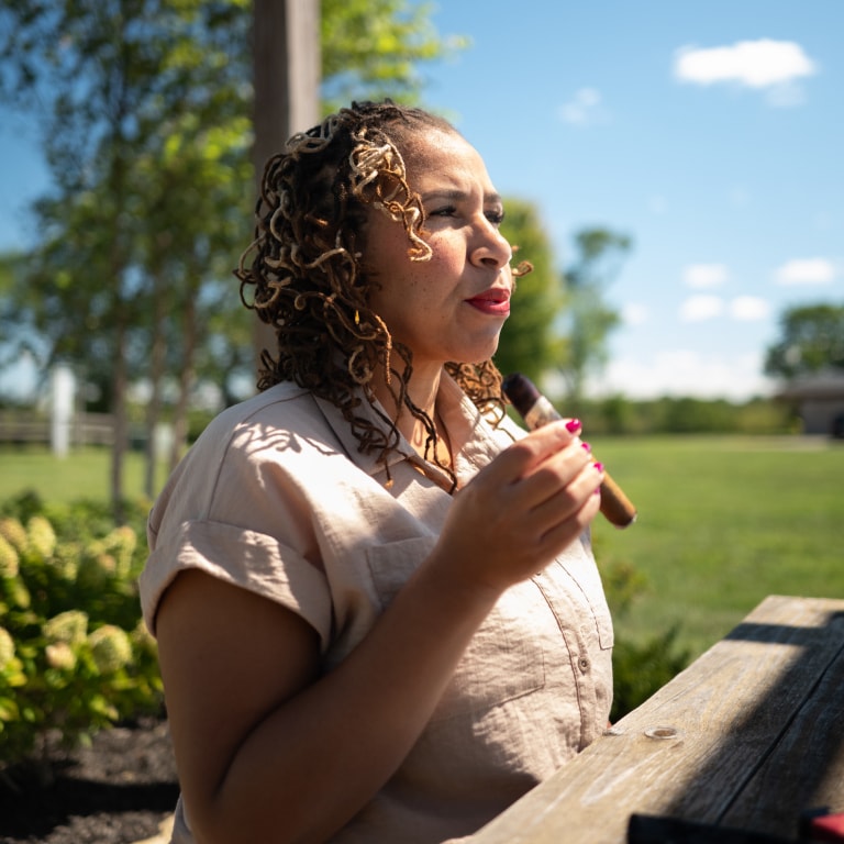 Relaxed moment from the Kentucky Castle Family Reunion showing a guest holding a cigar while seated outside under a clear sky with lush greenery.