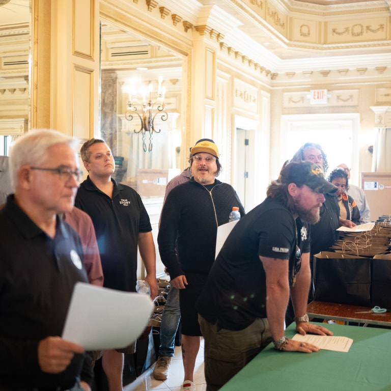 Participants at the Kentucky Castle Family Reunion at the registration desk in a grand room with ornate decor, chandeliers, and a mirrored wall.