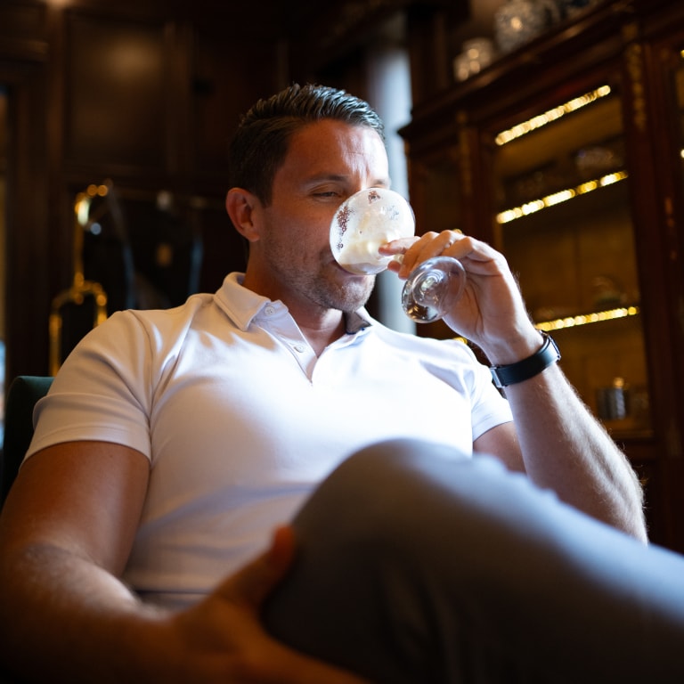 Guest at the Kentucky Castle Family Reunion sitting in a wood-paneled room, holding a glass and dressed in casual white and grey attire.