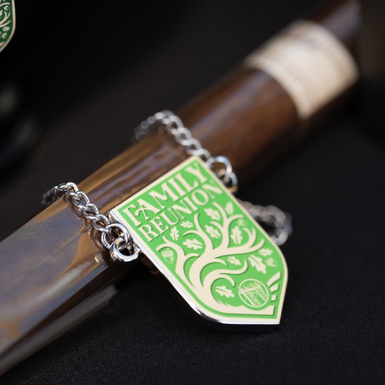 Close-up of a Kentucky Castle Family Reunion pendant with a leafy tree design and bold 'FAMILY REUNION' lettering, placed on a rustic wooden background.