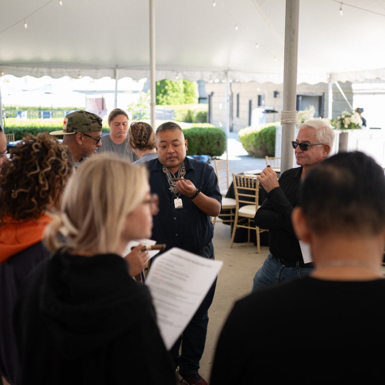 Group of people gathered under a tent at a Kentucky Castle Family Reunion, engaged in conversation and tasting some cigars, surrounded by chairs and tables in an outdoor setting.