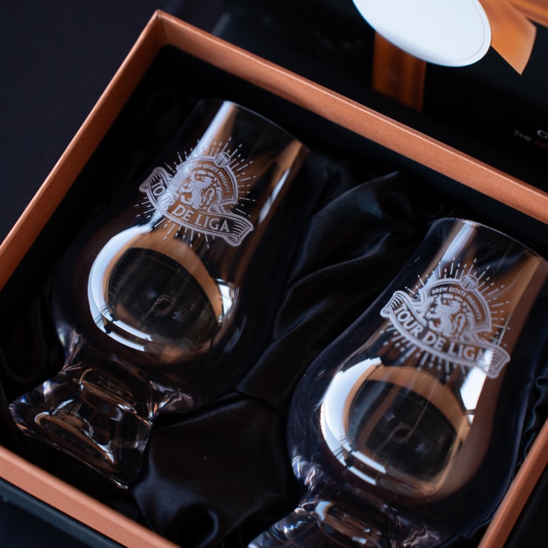 Elegant pair of clear crystal glasses engraved with the Tour de Liga lion emblem, highlighting the premium Tour de Liga Experience souvenirs.