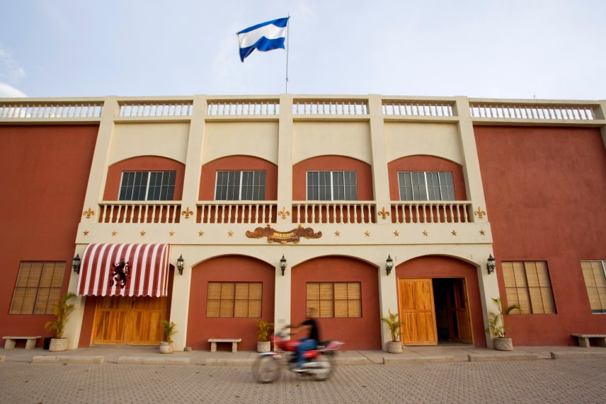 A motorcyclist speeds by a modern building with a flag, showcasing its sleek design and large glass panels