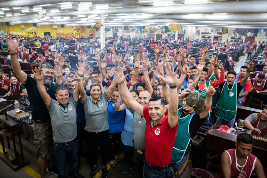 a group of workers in the cigar workshop holding their hands up with cheerful faces