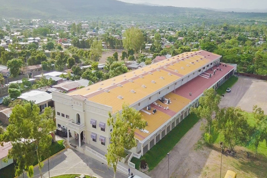 Aerial view of a large building featuring a distinct yellow roof, surrounded by greenery and other structures.