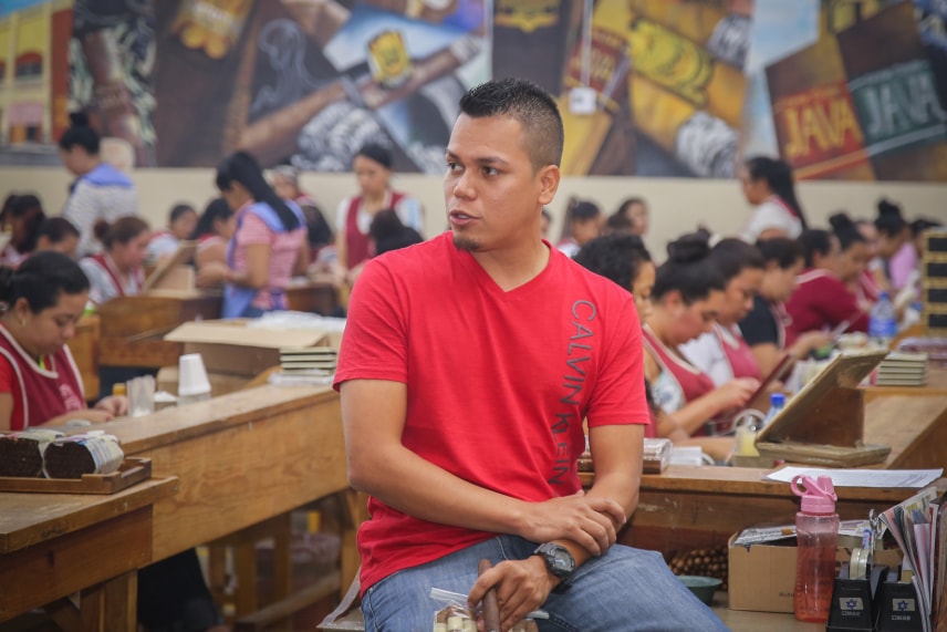 A man sits at a table surrounded by cigar factory workers