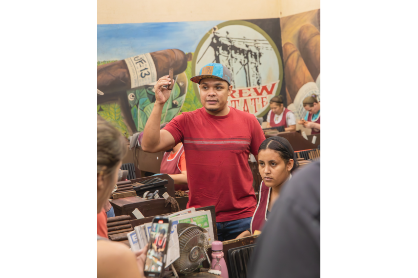 A man in a red shirt and blue hat stands in front of a group of people, engaging with them in conversation.