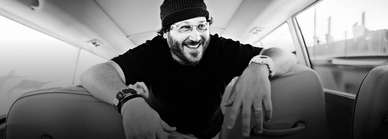 Black and white photo of Jonathan Drew leaning forward between two bus seats —capturing a candid, behind-the-scenes moment of the iconic cigar industry figure